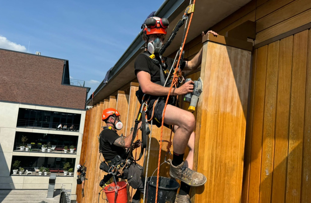 Urban building maintenance is a growing market — technicians with trade skills command better rates Two rope access technicians working on a timber façade in a city